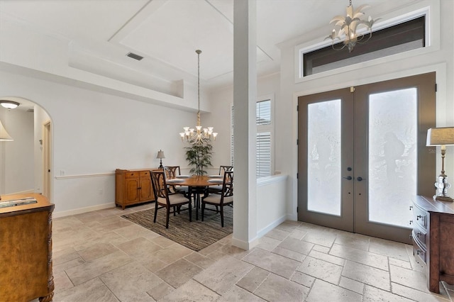 foyer featuring baseboards, arched walkways, an inviting chandelier, stone tile flooring, and french doors