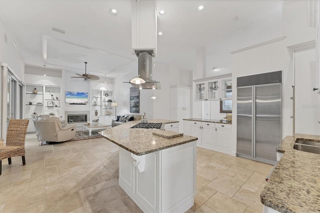 kitchen featuring ceiling fan, white cabinetry, stainless steel built in fridge, a glass covered fireplace, and stone tile flooring