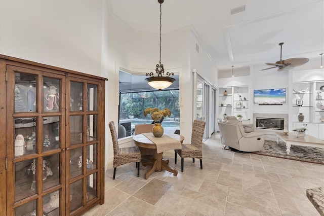 dining space featuring built in shelves, visible vents, a towering ceiling, a glass covered fireplace, and stone finish flooring