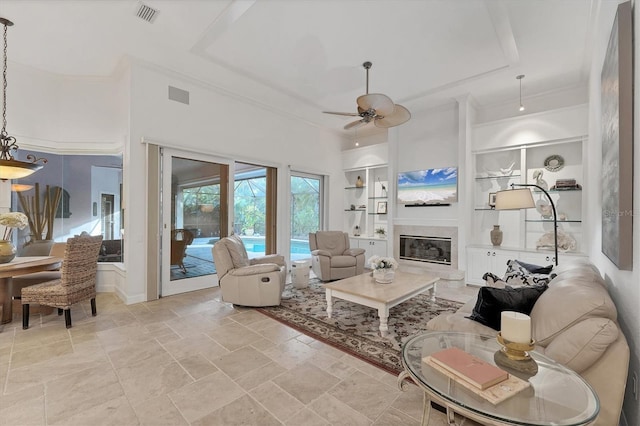 living area with built in shelves, visible vents, crown molding, and a glass covered fireplace