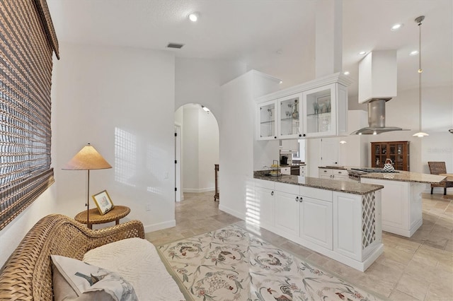 kitchen featuring arched walkways, a peninsula, a towering ceiling, visible vents, and white cabinets