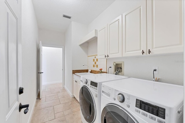 clothes washing area with washing machine and dryer, a sink, visible vents, cabinet space, and stone tile flooring