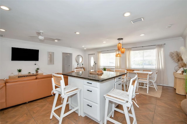 kitchen featuring decorative light fixtures, white cabinets, ornamental molding, a center island, and light parquet flooring