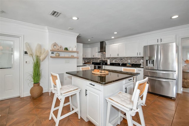 kitchen with a breakfast bar area, appliances with stainless steel finishes, white cabinets, a kitchen island, and wall chimney exhaust hood