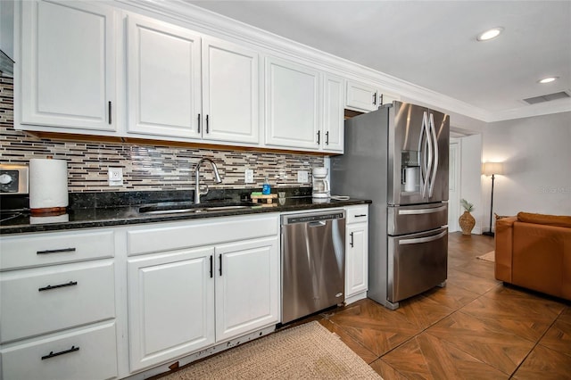 kitchen with sink, white cabinetry, crown molding, appliances with stainless steel finishes, and dark stone counters