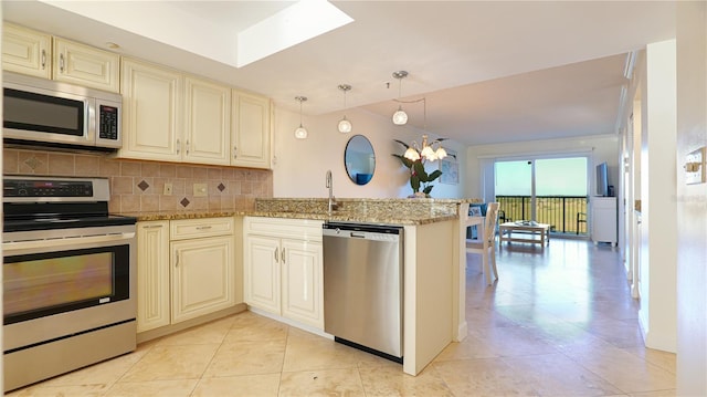 kitchen with a peninsula, appliances with stainless steel finishes, cream cabinets, and backsplash