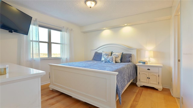 bedroom featuring light wood-type flooring, a textured ceiling, and baseboards