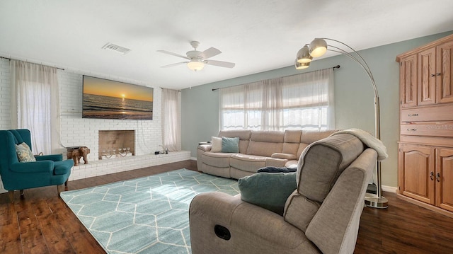 living room with a brick fireplace, dark wood-type flooring, and ceiling fan