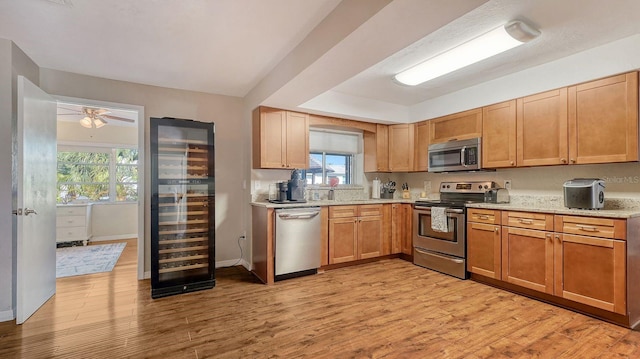 kitchen featuring sink, wine cooler, light stone counters, stainless steel appliances, and light wood-type flooring