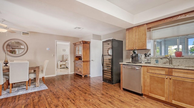 kitchen with sink, black fridge, stainless steel dishwasher, light hardwood / wood-style floors, and light stone countertops