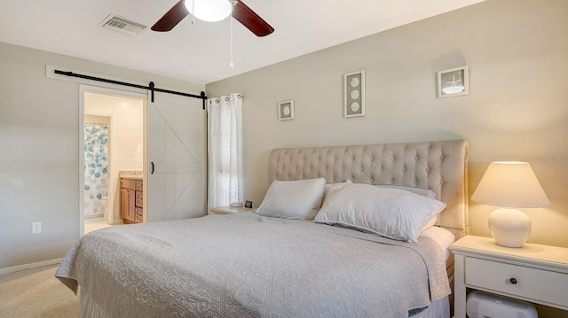 bedroom featuring ensuite bathroom, a barn door, light carpet, and ceiling fan