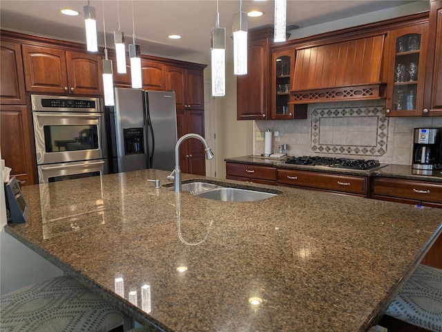 kitchen with decorative backsplash, appliances with stainless steel finishes, a breakfast bar, dark stone countertops, and a sink