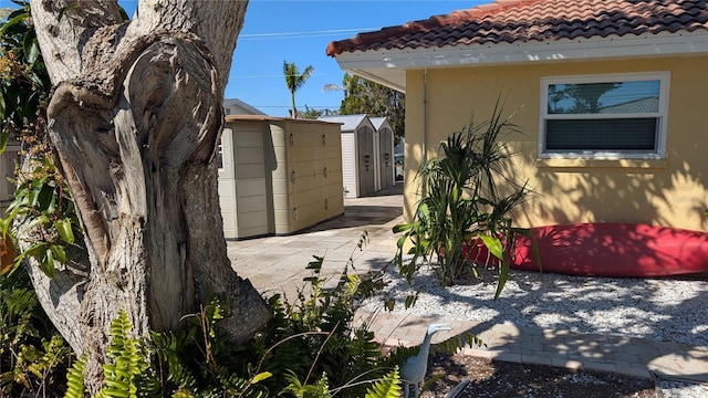 view of side of home with stucco siding, a shed, an outdoor structure, and a tiled roof