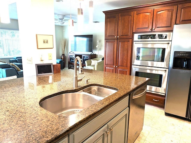 kitchen with ceiling fan, a sink, open floor plan, appliances with stainless steel finishes, and dark stone countertops