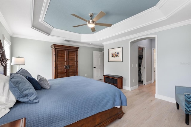 bedroom with crown molding, light hardwood / wood-style flooring, ceiling fan, a walk in closet, and a raised ceiling