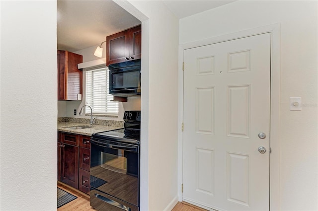 kitchen with light stone counters, sink, black appliances, and light hardwood / wood-style floors