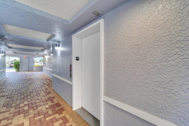 corridor with elevator and a textured ceiling