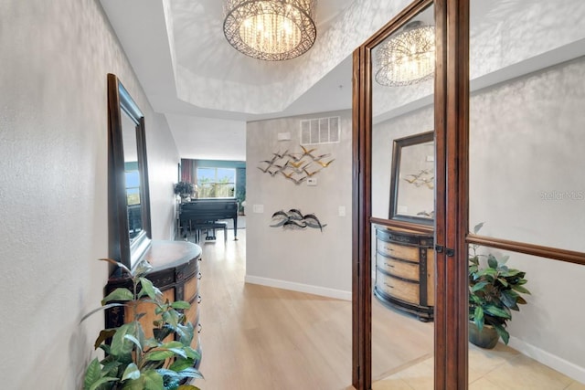 corridor featuring light hardwood / wood-style floors, an inviting chandelier, and a tray ceiling