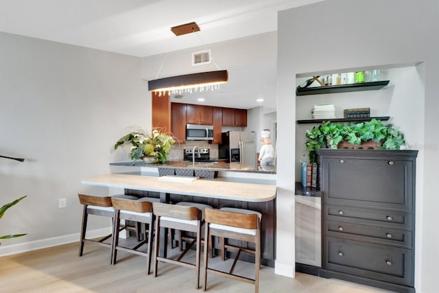 kitchen featuring decorative backsplash, appliances with stainless steel finishes, a breakfast bar, and kitchen peninsula