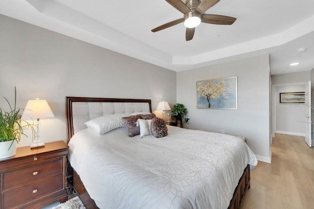 bedroom featuring a tray ceiling, ceiling fan, and light wood-type flooring