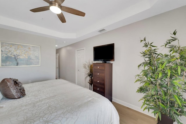 bedroom with ceiling fan, a raised ceiling, and wood-type flooring