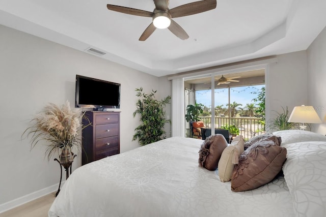 bedroom featuring a raised ceiling, light wood-type flooring, ceiling fan, and access to exterior