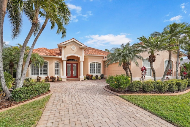 mediterranean / spanish-style house featuring decorative driveway, french doors, a tile roof, stucco siding, and an attached garage