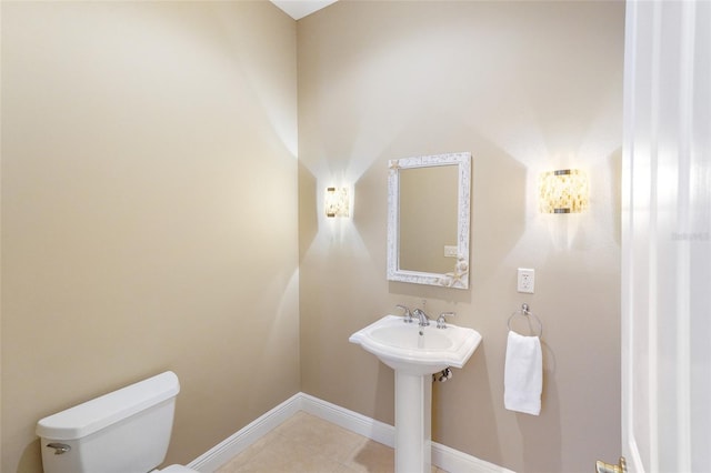 half bathroom with toilet, baseboards, a sink, and tile patterned floors