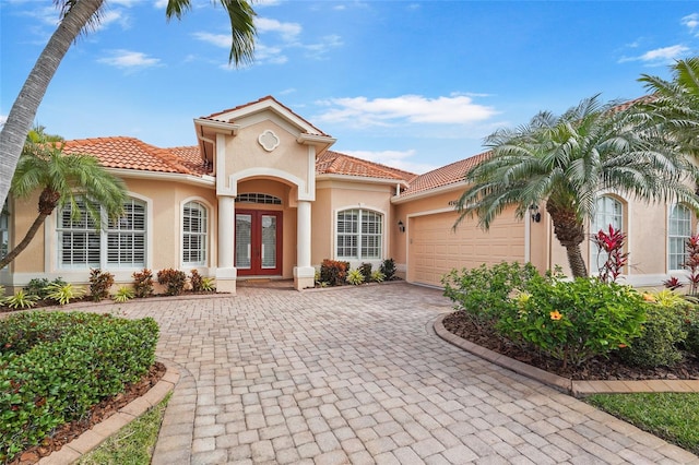 mediterranean / spanish house with decorative driveway, french doors, an attached garage, and stucco siding