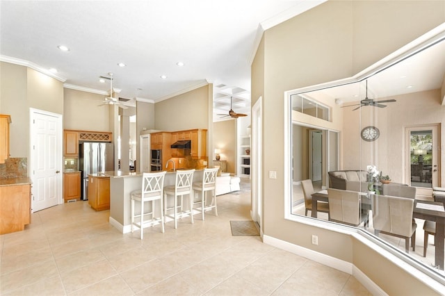 kitchen with stainless steel appliances, ornamental molding, open floor plan, under cabinet range hood, and a kitchen breakfast bar