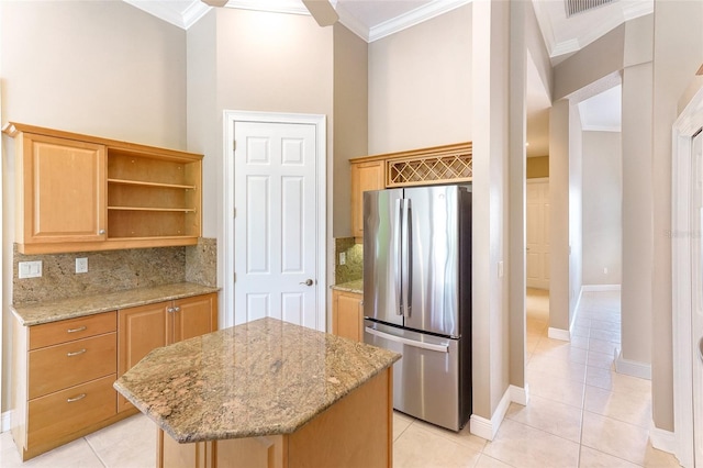 kitchen featuring light stone counters, a center island, freestanding refrigerator, decorative backsplash, and crown molding