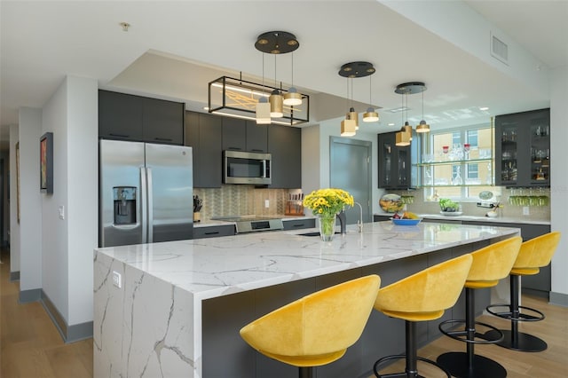 kitchen featuring pendant lighting, a large island, stainless steel appliances, light stone countertops, and decorative backsplash