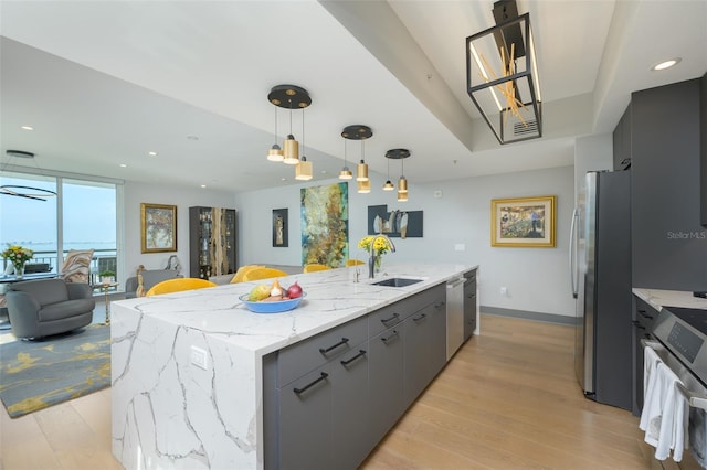 kitchen featuring sink, decorative light fixtures, appliances with stainless steel finishes, gray cabinets, and a kitchen island with sink