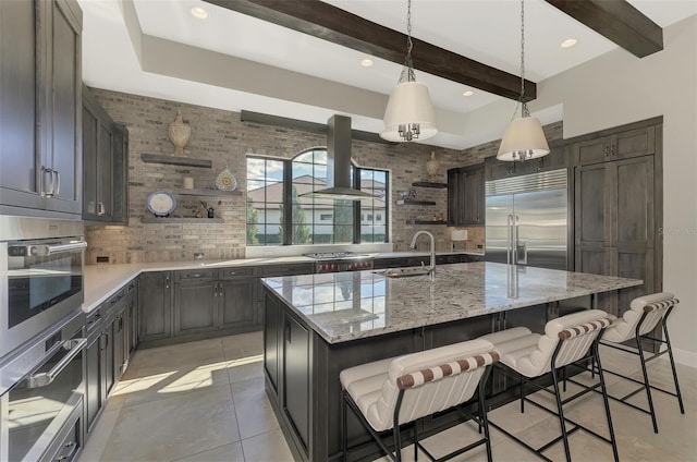 kitchen featuring open shelves, appliances with stainless steel finishes, a kitchen island with sink, a sink, and island range hood