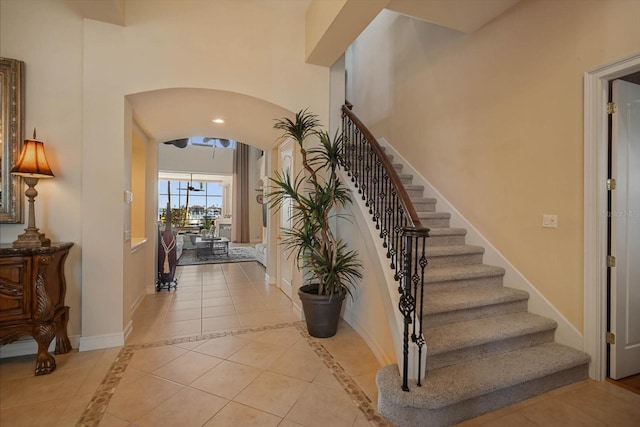 foyer featuring arched walkways, light tile patterned floors, a high ceiling, baseboards, and stairs