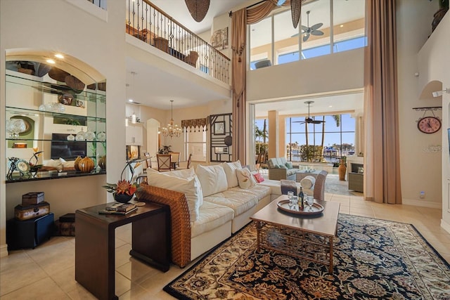 living room with ceiling fan with notable chandelier, light tile patterned flooring, a towering ceiling, and baseboards