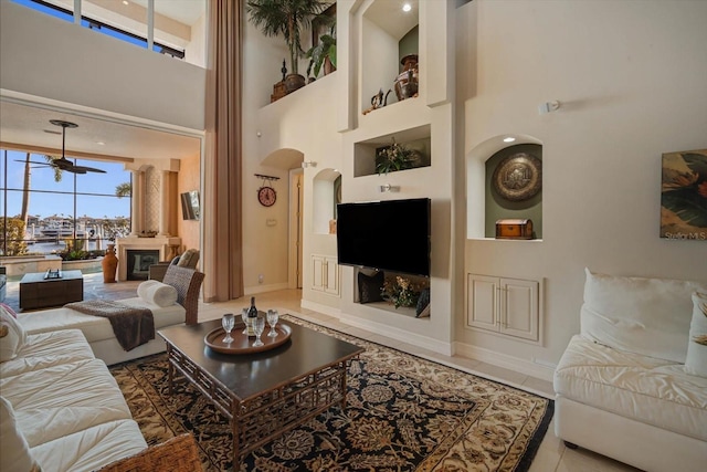 tiled living area featuring arched walkways, baseboards, ceiling fan, and a high ceiling