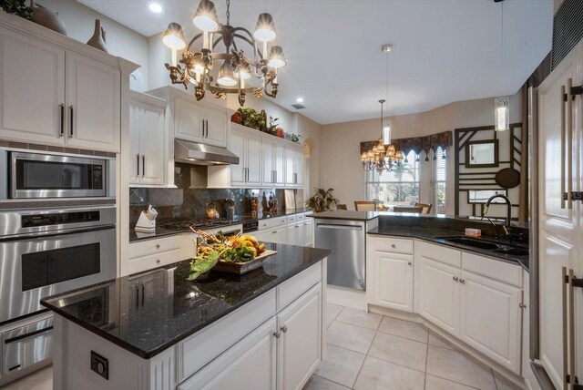 kitchen with a notable chandelier, under cabinet range hood, a sink, white cabinetry, and appliances with stainless steel finishes