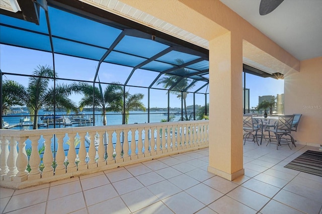 view of patio / terrace featuring glass enclosure, a water view, and a ceiling fan