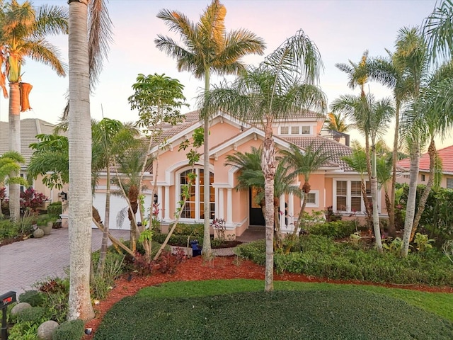 mediterranean / spanish-style home featuring a tile roof, a front yard, decorative driveway, and stucco siding