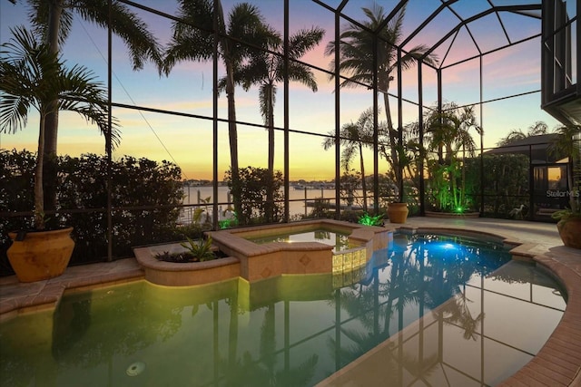 pool at dusk featuring a patio area, a water view, a lanai, and a pool with connected hot tub