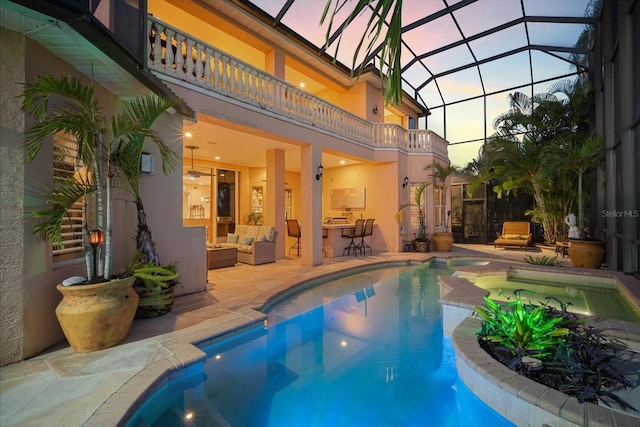 pool at dusk featuring glass enclosure, an outdoor pool, an outdoor hangout area, and a patio