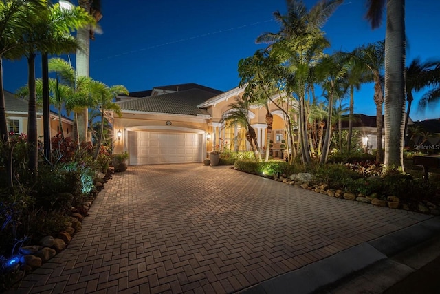 mediterranean / spanish house featuring a garage, a tile roof, decorative driveway, and stucco siding