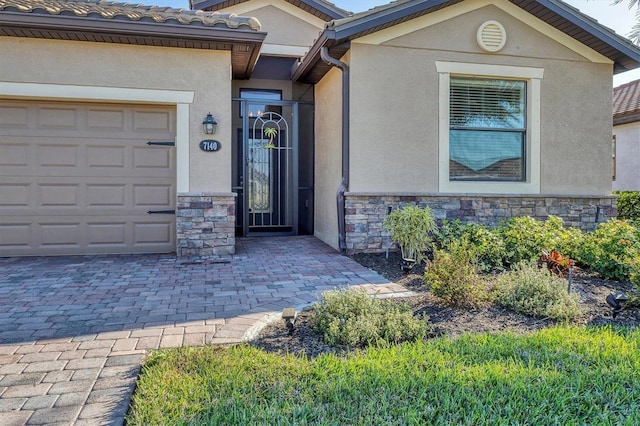 property entrance with decorative driveway, a tile roof, stucco siding, a garage, and stone siding