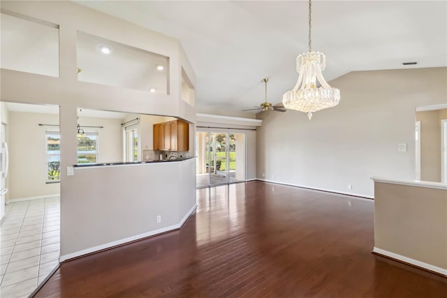 unfurnished living room with hardwood / wood-style floors, ceiling fan with notable chandelier, and high vaulted ceiling