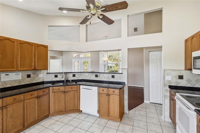 kitchen featuring light tile patterned flooring, sink, dark stone countertops, backsplash, and white appliances