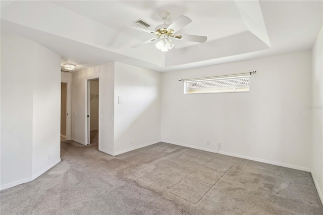 spare room featuring ceiling fan, light colored carpet, and a raised ceiling