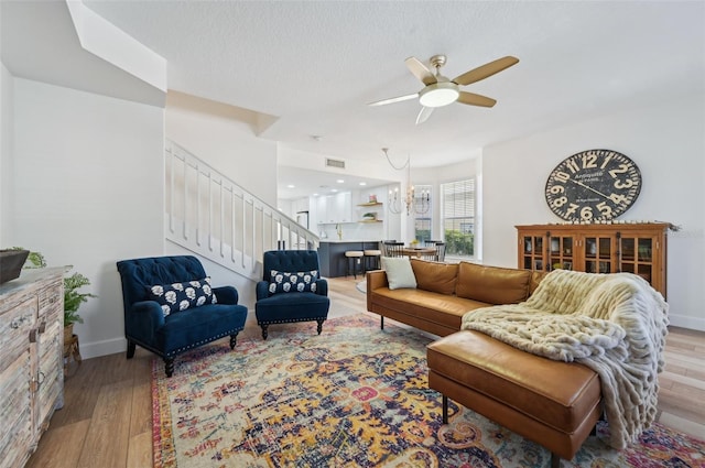 living room with ceiling fan with notable chandelier, light hardwood / wood-style flooring, and a textured ceiling