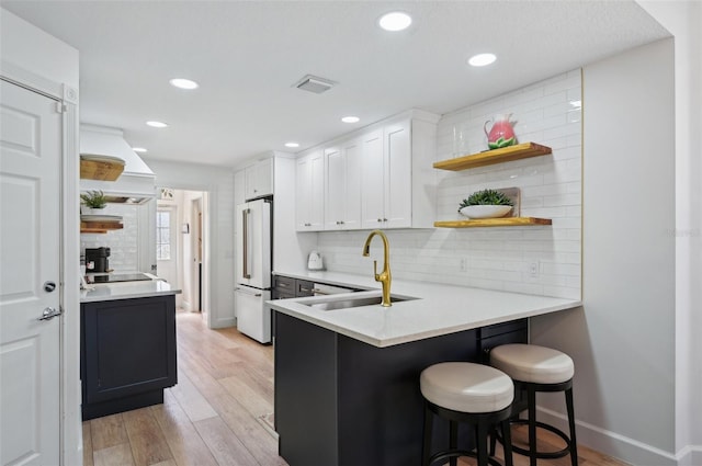 kitchen featuring high quality fridge, white cabinets, a kitchen bar, custom exhaust hood, and kitchen peninsula