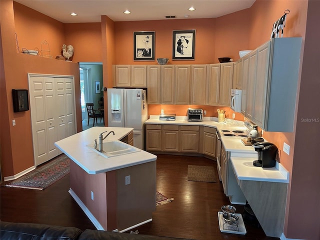 kitchen with dark hardwood / wood-style floors, a towering ceiling, sink, a center island with sink, and white appliances